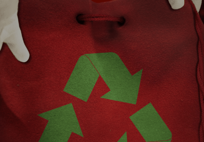 Santa holding a red bag with a green recycling icon on it