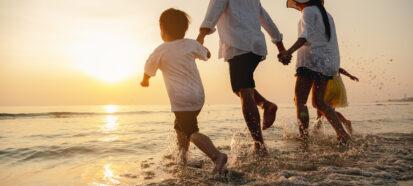 image of a family consisting of a sogn, father, mother and daughter, running having fun ona. beach in the evening